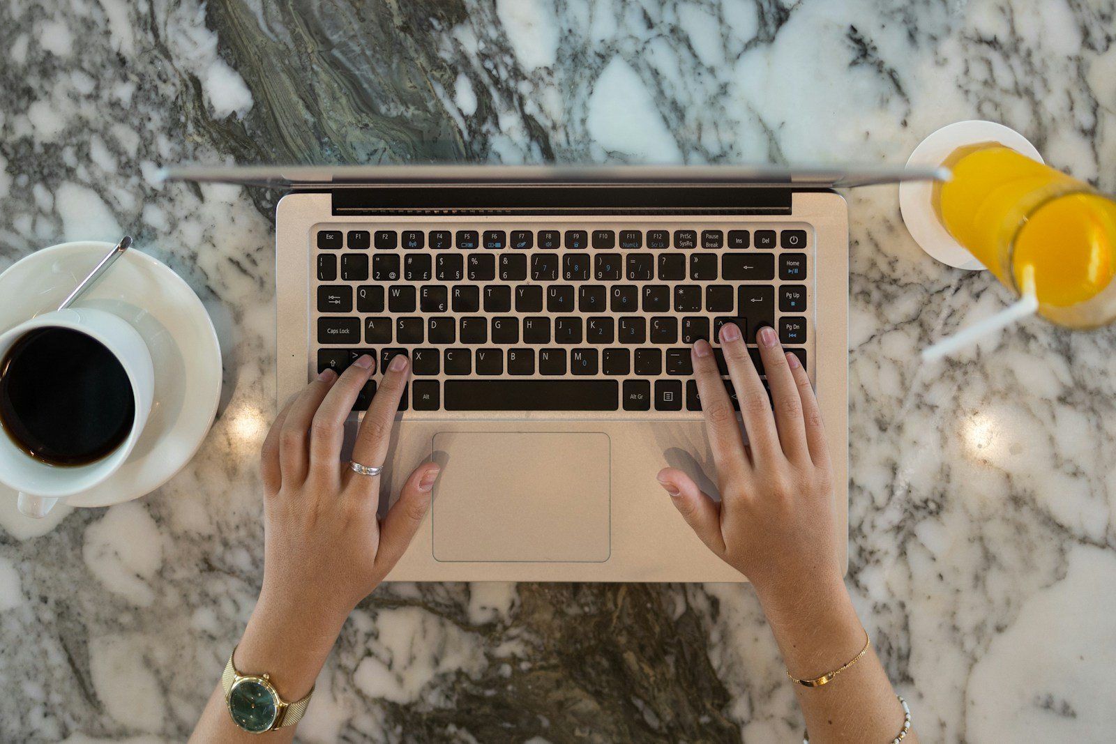 A top-down workspace scene with a laptop, coffee and orange juice on a marble table