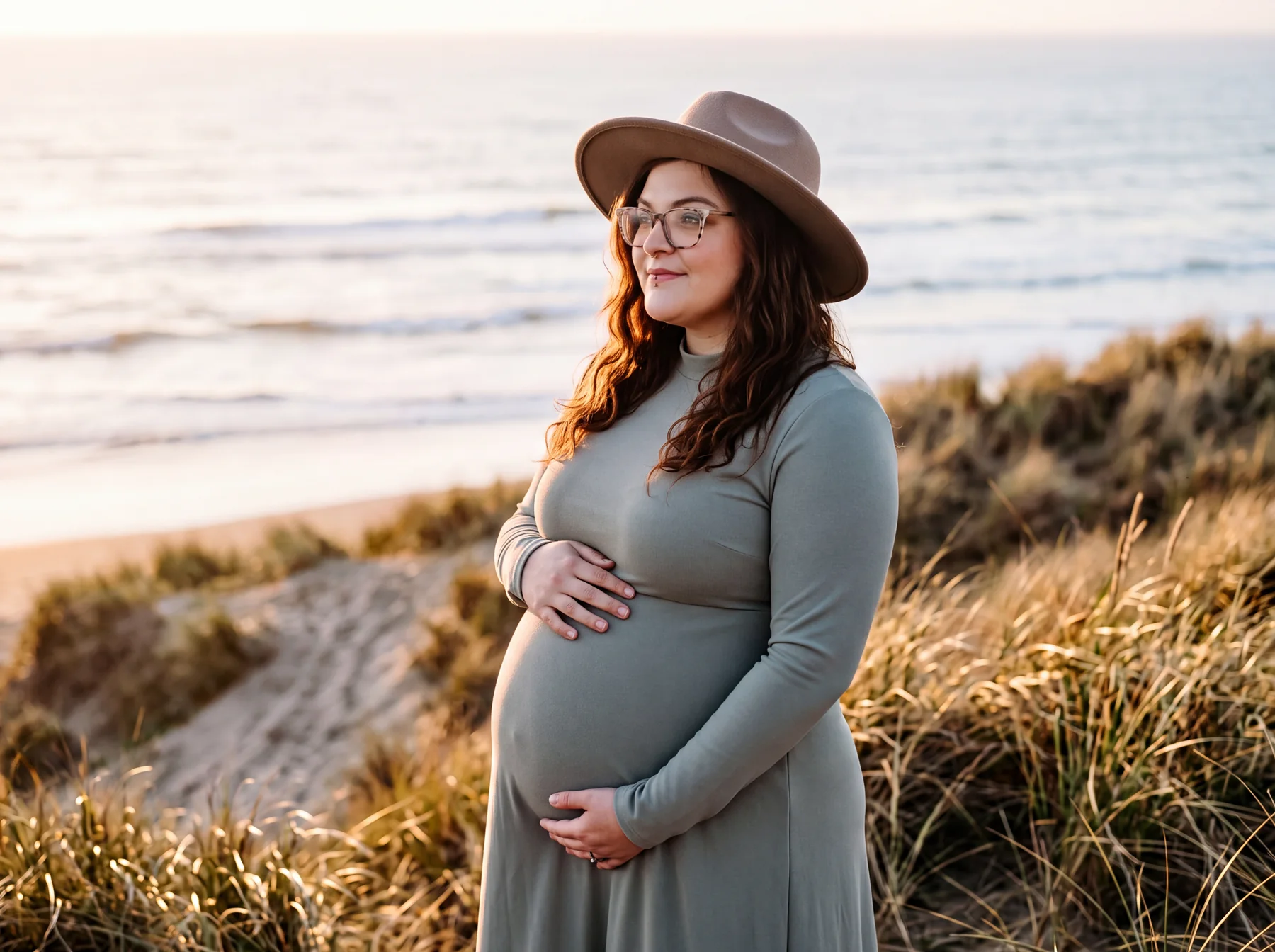 An expectant mother wearing a hat among pale beach grasses