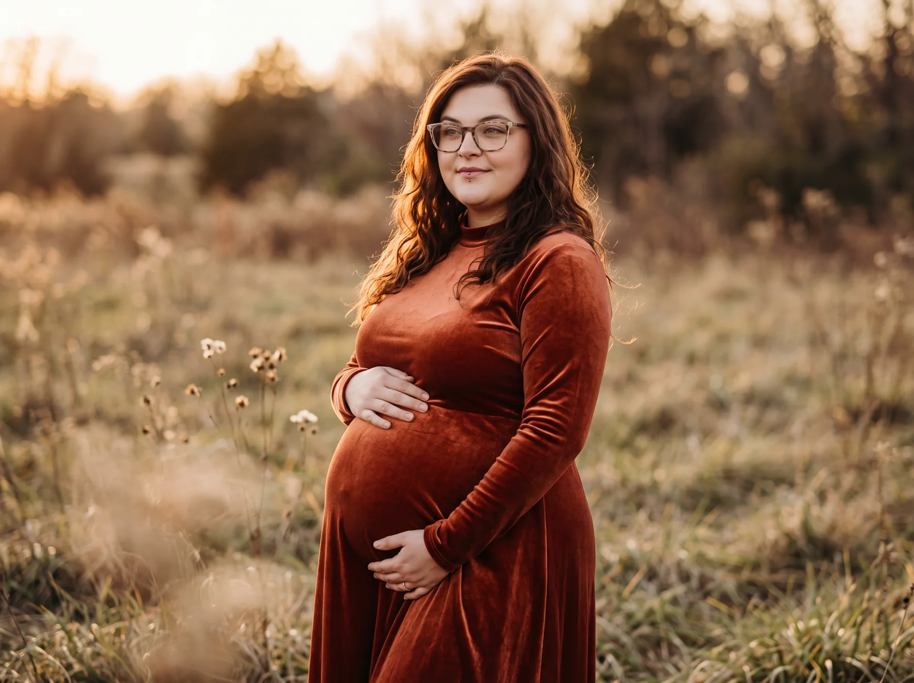 An expectant mother in a rust velvet dress in a golden meadow